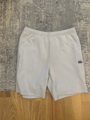 Vita shorts från Lacoste - Snygga vita shorts från Lacoste med elastisk midja och det klassiska krokodilmärket på vänster ben. Tillverkade i mjukt bomullsmaterial för en bekväm känsla. Perfekta för sommardagar eller chill hemma.