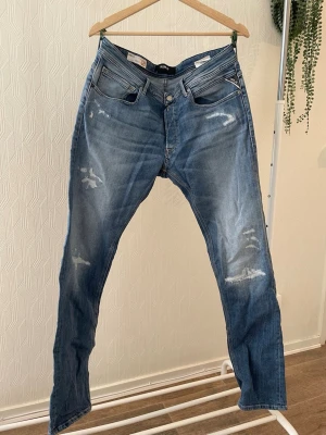 Blå slim fit jeans från replay - Snygga blå jeans från replay i regular slim fit-modell. Jeansen har slitningar och detaljer på benen som ger en cool look. Materialet är denim och modellen Replay 573 BIO. Perfekt för dig som gillar trendiga och bekväma jeans.