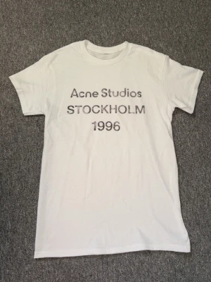 Acne Studios t-shirt - Riktigt fet och eftertraktad T-shirt med Acne Studios loggan i storlek S. Riktigt bra skick! Obs: Lite osäker på äktheten då lappen i nacken saknas, därför säljs den billigare (349 kr, nytt pris ca 3000 kr. Längd cirka 65 cm, bredd cirka 44 cm. Tveka inte på att höra av dig vid minsta fundering! 🙌