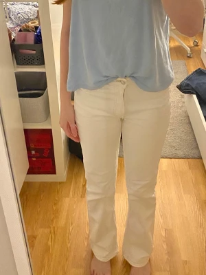 Vita raka jeans med hög midja - Säljer ett par vita jeans med rak passform och hög midja. Jeansen har klassisk femficksdesign och stängs med knapp och dragkedja. Perfekta till både vardag och festliga tillfällen.