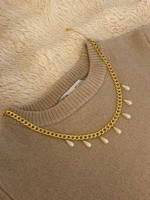 Guldhalsband med droppformade pärlor - Snyggt halsband i guldfärgad rostfritt med droppformade vita pärlor som hänger längs kedjan. Perfekt accessoar för att lyfta vilken outfit som helst med en elegant touch. Kedjan har en klassisk design och pärlorna ger en trendig vibe.