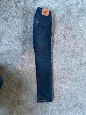 Levi's blå slim jeans - Säljer ett par klassiska blå jeans från Levi's med slim passform och hög midja. Jeansen har fem fickor. Finns även möjlighet för att justera hårdheten på midjan genom resårband på insidan av jeansen