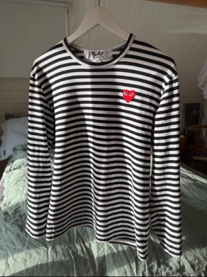 Randig långärmad tröja Comme des Garçons - Säljer en svartvit randig långärmad tröja från Comme des Garçons PLAY med det ikoniska röda hjärtat med ögon broderat på bröstet. Tröjan har rund hals och är gjord i mjukt bomullsmaterial. Perfekt för dig som vill ha något trendigt. Den är i storlek L men sitter mer som en M hör av dig vid övriga frågor 