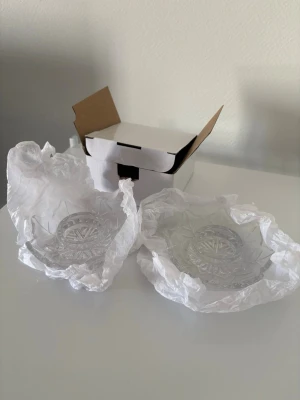 Två små ljuslyktor i glas - Säljer två genomskinliga ljuslyktor i glas med dekorativt mönster. De har en rund form med stjärnliknande kanter och levereras i originalförpackning. Perfekta som dekoration eller för värmeljus.