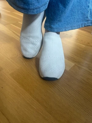 Vagabond sneakers i storlek 38 - Säljer fina snygga beige Vagabond slip-on sneakers med stickad mesh-överdel och elastisk mudd runt ankeln. Skorna har en minimalistisk design utan snörning och en vit sula med svart detalj framtill. Perfekta för en clean och modern look.Storlek 38