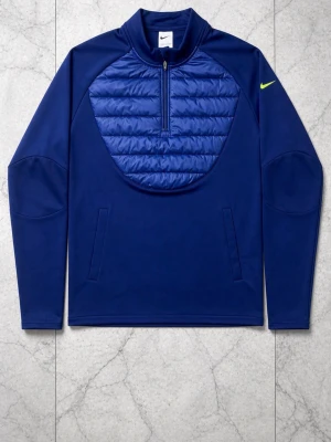 Blå träningsjacka från Nike - Snygg blå träningsjacka från Nike med quiltad panel på bröstet och halv dragkedja. Jackan har två sidofickor och en gul Nike-logga på ärmen. Perfekt för löpning eller gym. Materialet är mjukt och stretchigt, med extra vaddering framtill.