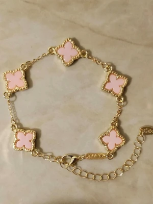 Guldfärgat armband med rosa blommor - Snyggt armband i guldfärg med fem fyrklöverformade länkar i ljusrosa emalj. Kedjan är tunn och justerbar med karbinlås✨