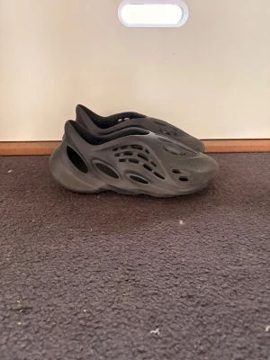 Foamrunners - Säljer ett par svarta tofflor i skumplast med modern, futuristisk look och många ventilationshål. De har en chunky sula och är superlätta att bära. Perfekta för dig som gillar streetwear och vill ha något unikt på fötterna.