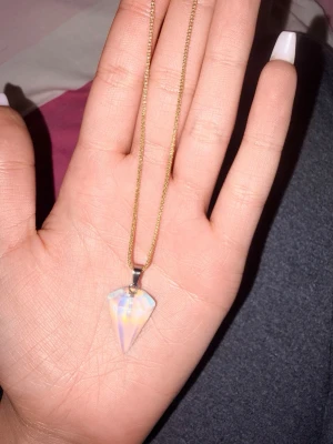 Halsband med opalitspets - Snyggt halsband med en kedja i guldton och ett hängsmycke i form av en spetsig opalitsten. Hängsmycket har en skimrande, nästan regnbågsfärgad yta som skiftar i blått och vitt. Perfekt accessoar för att lyfta din stil.