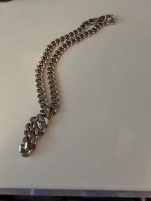 Silverfärgat kedjehalsband - Stilrent halsband i silverfärg med breda, platta länkar. Kedjan har en klassisk design och passar perfekt till en trendig look. Materialet ser ut att vara metall och halsbandet har ett robust intryck. Perfekt accessoar för att lyfta din outfit.