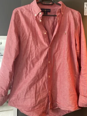 Rosa skjorta från Ralph Lauren XL - Säljer en snygg rosa skjorta från Ralph Lauren i storlek XL. Skjortan har klassisk button-down krage, långa ärmar och knappar framtill. Materialet är bomull och den har den ikoniska loggan broderad på bröstet. Perfekt för dig som gillar stilrena plagg.