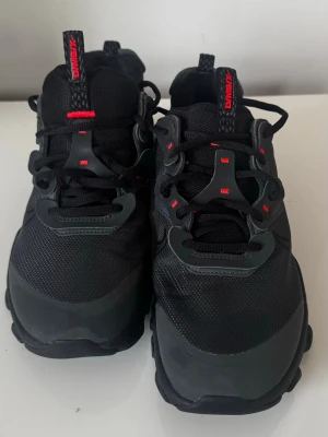 Nike React Vision sneakers - Svarta sneakers från Nike React Vision D/MS/X i stl 40 med coola röda detaljer på snörningen och loggan. Använda endast ett fåtal gånger. Skorna har en sportig design med mesh och syntetmaterial i ovandelen samt en robust sula som ger bra grepp. Perfekt för dig som gillar en aktiv och modern look.