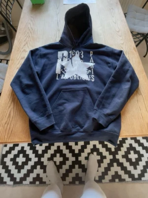 Mörkblå  zandrostudio hoodie - Mörkblå hoodie med stor vit tryckt design på bröstet där det står bland annat 'Paris', '1983' och 'L RÉPUBLIQUES'. Hoodien har en klassisk känguruficka framtill och justerbar huva med snören. Perfekt för en avslappnad streetwear-look.