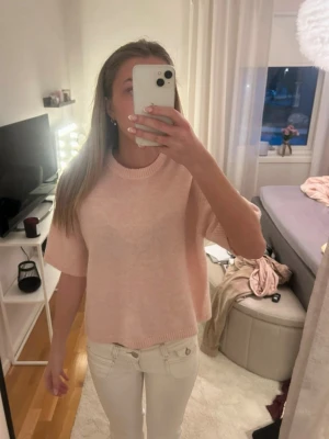Ljusrosa stickad t-shirt - Säljer en ljusrosa stickad t-shirt med korta ärmar och rund halsringning. Tröjan är mjuk och har en avslappnad passform, perfekt för lager-på-lager eller sommarens svalare dagar.