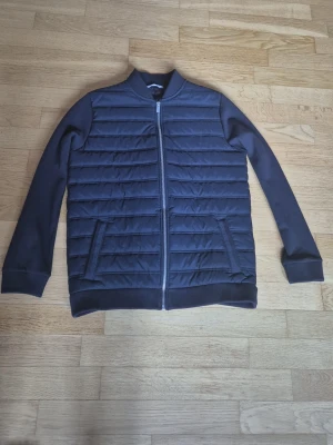 M and S bomber jacket - Snygg mörkblå bomberjacka med quiltat mönster på fram- och baksida samt släta ärmar. Jackan har dragkedja framtill, ribbade muddar och två snedställda fickor. Perfekt för dig som vill ha en stilren och modern look. Varan har inga defekter alls