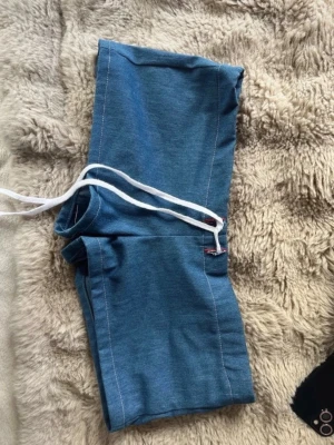 Blåa shorts med snörning - Snygga blåa shorts med vit snörning i midjan. Modellen är lågmidjad och har en sportig look, perfekta för sommarens varma dagar. Tillverkade i ett mjukt och bekvämt material som passar till avslappnade outfits.