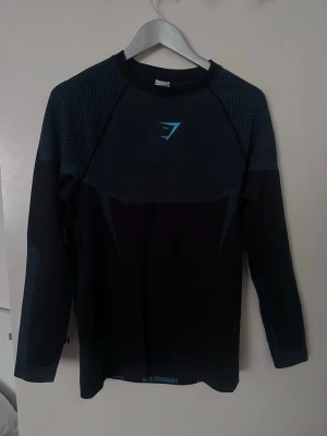 Onyx v5 Gymshark - Säljer en svart långärmad träningströja från Gymshark med blå detaljer och logga på bröstet. Tröjan har ett sportigt snitt och är tillverkad i ett stretchigt och ventilerande material som passar perfekt för gym och löpning.
