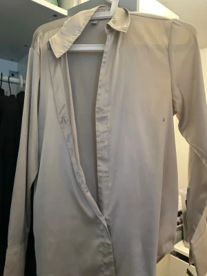 Beige klassisk skjorta med knappar - En stilren beige skjorta med klassisk krage och knappar hela vägen ner. Skjortan har långärmad design och är tillverkad i ett tunt, mjukt material som känns skönt mot huden. Perfekt för dig som gillar en enkel och clean look.