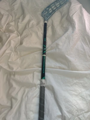 OxDog blå innebandyklubba - Innebandyklubba från OxDog med blått skaft och ljusblått blad. Greppet är grått och det finns vit tejp runt handtaget. Klubban är en väldigt najs innebandy klubba inte skadad eller nåt och har en modern design som passar för innebandyspel.