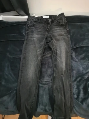 Svarta slim fit jeans från newyorker  - Säljer ett par svarta slim fit jeans från Weekday med snyggt slitna detaljer och klassisk femficksdesign. Jeansen har dragkedja och knapp framtill samt raka ben. Perfekt för dig som gillar en modern och avslappnad look.