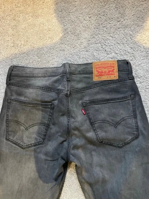 Dark fade Levis jeans - Jeans med mörkgrå cool fade i storlek w32 l30. De är i modellen 502 som man ser på bilderna vilket är en tapered fit, slim/ raka jeans med andra ord som smalnar av.