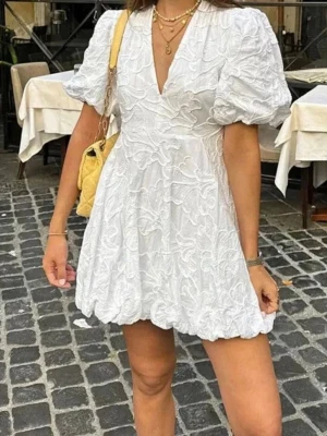 Vit kortklänning med puffärm - Supersöt vit kortklänning med puffärmar och v-ringning. Finns ett hål i armhålan då den kom så när jag fick hem den från hemsidan, inget som syns eller märks, går säkert att fixa med några stygn. Aldrig använd