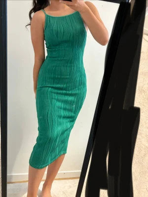 Grön ribbad midiklänning - Snygg grön midiklänning med smala axelband och ribbad struktur. Klänningen är figurnära och har ett vågigt mönster i tyget som ger en cool look. Perfekt för dig som gillar stilrena och trendiga plagg.