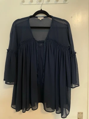 Marinblå omlottblus volanger - Fluffig och luftig marinblå blus med omlott-design och knytband framtill. Blusen har vida trekvartsärmar och är tillverkad i ett transparent, lätt material som ger ett bohemiskt intryck. Perfekt för sommarens varma dagar. Denna är för liten för mig så därför väljer jag att sälja den😊 Strl 6/32