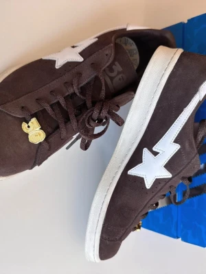 Bruna BAPE x Adidas Campus sneakers Storlek 43 - Snygga bruna sneakers i mocka från BAPE och Adidas med vit stjärndetalj på sidan och guldfärgade detaljer vid snörningen. Klassisk låg modell med vit sula och ikoniska samarbetet tryckt på sidan. Perfekta för dig som gillar streetwear och unika samarbeten Storlek 43 och är i väldigt bra skick. Pris kan diskuteras, hör av dig ! 🤙 .