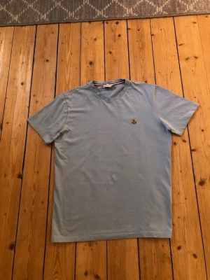 Ljusblå t-shirt från Moncler - Säljer en stilren ljusblå t-shirt från Moncler med rund hals och korta ärmar. T-shirten har en liten Moncler-logga på bröstet och är gjord i mjuk bomull för en skön känsla. Perfekt för dig som gillar minimalistisk design.