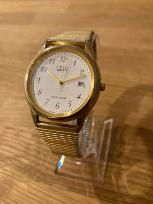 1992 Citizen Gold Plated Mesh 36mm Herrur - Citizen Quartz armbandsur med ett guldpläterat boett och ett mesharmband i två toner. Urtavlan är vit med arabiska siffror och har en datumvisning vid klockan 3. Klockan är märkt ”WATER RESIST” på urtavlan och ”STAINLESS STEEL” på baksidan av boetten och armbandets lås. Fint skick enligt bilder med fungerande batteri! Modell: 270450, 1112-5782.  Begagnat värde: 400+ SEK Mitt pris: 389 SEK  Skickas alltid snabbt och spårbart. Skriv vid frågor och se gärna mina andra annonser!   GRATIS: För återko