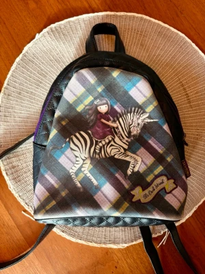Santoro Gorjuss mini ryggsäck "The DarkStreak" - Söt och unik mini-ryggsäck från Santoro Gorjuss med motivet "The Dark Streak" (flicka på zebra).        I väldigt fint skick/oanvänd!💕                                 Den har justerbara axelband Original Santoro London✨ Inuti är den randig och rymlig trots sin storlek! Längd: 22cm Bredd: 20cm