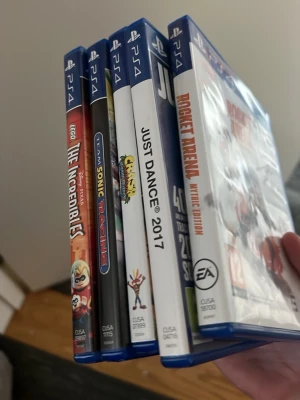 PS4 spelpaket med fem titlar - Säljer ett paket med fem PS4-spel: LEGO The Incredibles, Team Sonic Racing, Crash Bandicoot N. Sane Trilogy, Just Dance 2017 och Rocket Arena Mythic Edition. Alla spel kommer i blå plastfodral med originalomslag och färgglada illustrationer.