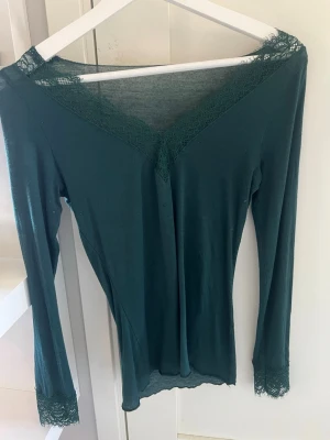 Mörkgrön långärmad Intimissimi-tröja storlek S - Mörkgrön långärmad Intimissimi tröja, V-ringad och spets. Har används några gånger. Litet hål på vänster sida. Sval och fin tröja att styla till sommarkvällarna 🌺💚