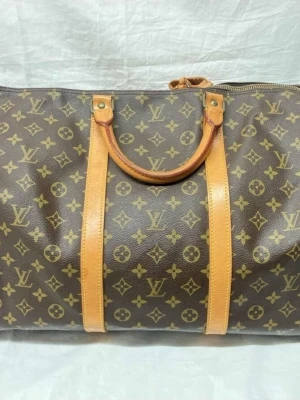 Louis Vuitton keepall 60 - Säljer en klassisk Louis Vuitton resväska i brunt monogrammönster med ljusbruna läderdetaljer och handtag. Väskan har en avlång form och dragkedja upptill. Perfekt för weekendresor och har ikoniska LV-loggan över hela väskan.