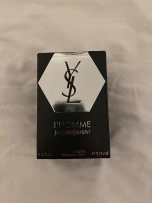 Yves Saint Laurent L'Homme Eau de Toilette - Säljer en lyxig parfym, L'Homme Eau de Toilette från Yves Saint Laurent. Flaskan är 100 ml och kommer i en elegant svart kartong med silverdetaljer och YSL-loggan. Perfekt för dig som vill ha en modern och maskulin doft.