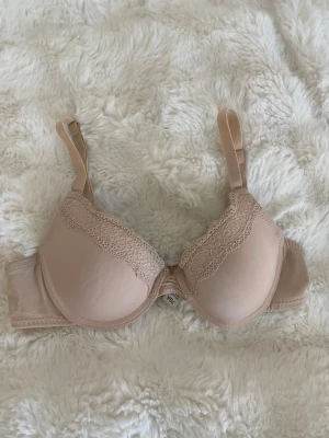 Beige BH 70A - Säljer denna beiga/ljusrosa BHn i storlek 70 A. Snygga spetsdetaljer framtill. Knappt använd så inga defekter eller annat. Vet tyvärr inte vad den är ifrån 