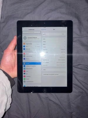 Apple iPad 4:e generationen - Säljer en Apple iPad 4e generationen med svart framsida och silverfärgad baksida. Surfplattan har en klassisk rektangulär form med rundade hörn och stor pekskärm. Baksidan är i aluminium med Apple-loggan och texten 'iPad'. Perfekt för surf, appar och media.