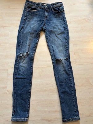 Blå odd Molly jeans - Säljer ett par blå skinny jeans med slitningar och hål på knäna. Jeansen är tillverkade i denim med stretch. Perfekt för dig som gillar en avslappnad och trendig look.