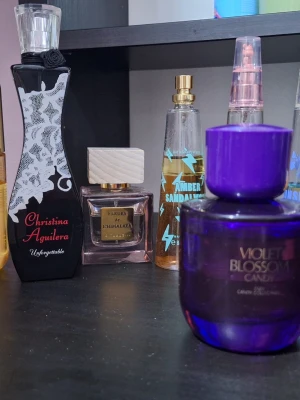 Christina Aguilera Unforgettable parfym set parfymer - Säljer en Christina Aguilera Unforgettable parfym i en elegant svart flaska med vita spetsdetaljer och röd text. Flaskan har en smal, kurvig form och en genomskinlig kork med svart blomdetalj. Perfekt för dig som gillar feminina och lyxiga dofter.