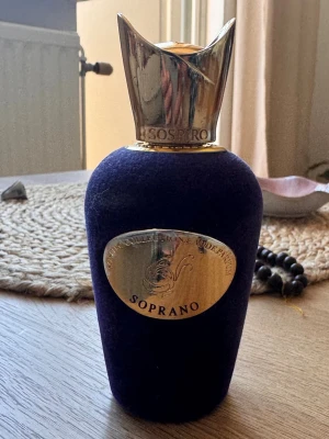 Sospiro Soprano 85/100 ml  - Discontinued.Exklusiv parfym från Sospiro med namnet Soprano. Flaskan är mörklila med en lyxig sammetsfinish och har en elegant guldfärgad metallkork. Den ovala guldfärgade etiketten framtill ger en premiumkänsla. Perfekt för dig som vill ha något unikt och stilfullt. 