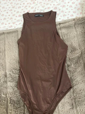 Brun body från SHEIN - Säljer en enkel och stilren brun body från SHEIN i storlek S. Bodyn har ärmlös design och rund halsringning, tillverkad i ett slätt och stretchigt material som sitter snyggt på kroppen. Perfekt att matcha med jeans eller kjol.