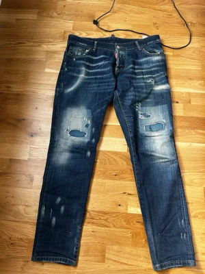 Dsquared2 distressed jeans blå - Coola blå jeans från Dsquared2 med slitningar och patchade detaljer på knäna. Jeansen har en klassisk femficksdesign, kontrastsömmar och en snygg vintage-wash. Perfekt för dig som gillar en edgy och trendig look.