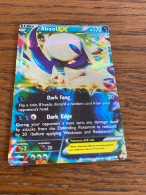 Pokémonkort Absol EX holografisk - Säljer ett coolt holografiskt Pokémonkort med Absol EX. Kortet har färgstarka motiv i blått, lila och gult, och är tillverkat i laminerad papp. Perfekt för samlare eller dig som vill boosta din lek med en stark EX Pokémon.