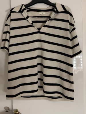 Randig kortärmad topp från H&M - Säljer en vit och svart randig topp från H&M med krage och v-ringning. Toppen har korta ärmar och är gjord i mjuk frotté. Använd väldigt få gånger, inga tecken på användning 💕💕