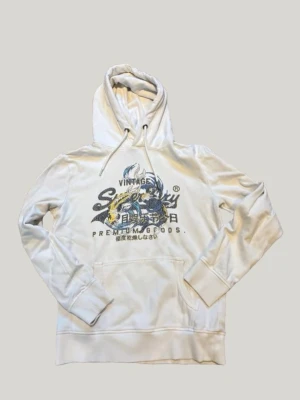 Superdry vintage tokyo hoodie  - En superdry vintage tokyo hoodie med snören, hoodien är i normal passform och är perfekt för en avslappnad fit. Färgen är något mellan beige och vit 