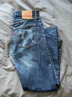 Levi's 501 blå jeans - Klassiska Levi's 501 jeans i blå denim med vintage känsla och. Rak passform läderpatch bak. Lite slitna på framsidan.