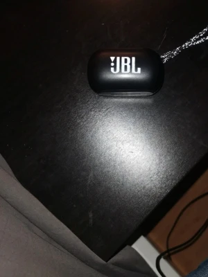 JBL svarta trådlösa in-ear hörlurar - Säljer ett par svarta trådlösa in-ear hörlurar från JBL med laddningsetui. Snygg och kompakt design med JBL-logga på både etui och hörlurar. Perfekta för musik, poddar och samtal. Laddas enkelt i det medföljande etuiet.