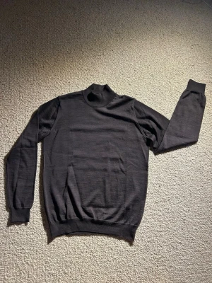Svart polotröja från Oscar Jacobson - Klassisk mörkbrun stickad polotröja från Oscar Jacobson. Tillverkad i Italien med mjukt och tunt material, perfekt för lager på lager. Tröjan har ribbade muddar vid ärmslut och nederkant samt en hög krage för extra stilpoäng. Kan inte tyda att den varit använd men har burits ett fåtal gånger. Nypris runt 1500kr och den klassas solklart vara i toppskick. 