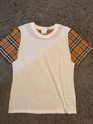 Burberry T-shirt - Snygg och stilren vit T-shirt från Burberry i högkvalitativ bomull. Tröjan har de ikoniska Burberry-rutorna. L passar M